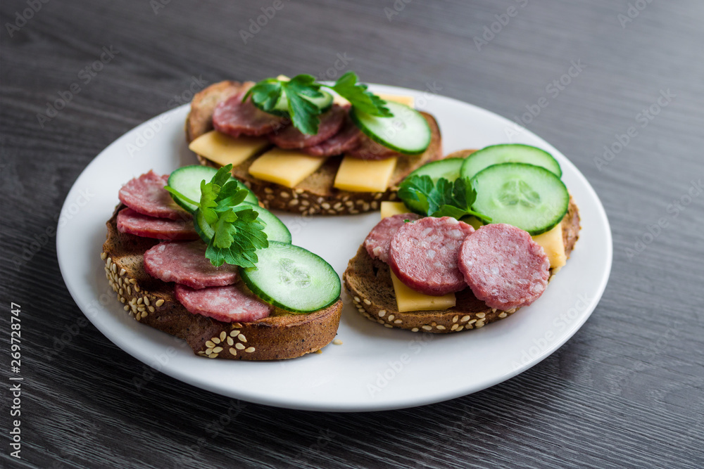 open sandwiches with salami cheese cucumber cheese parsley on white plate