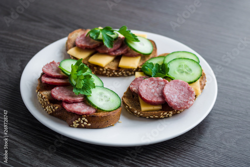 open sandwiches with salami cheese cucumber cheese parsley on white plate