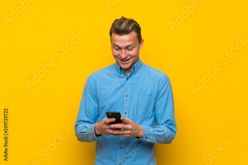 Blonde man over isolated yellow wall surprised and sending a message © luismolinero