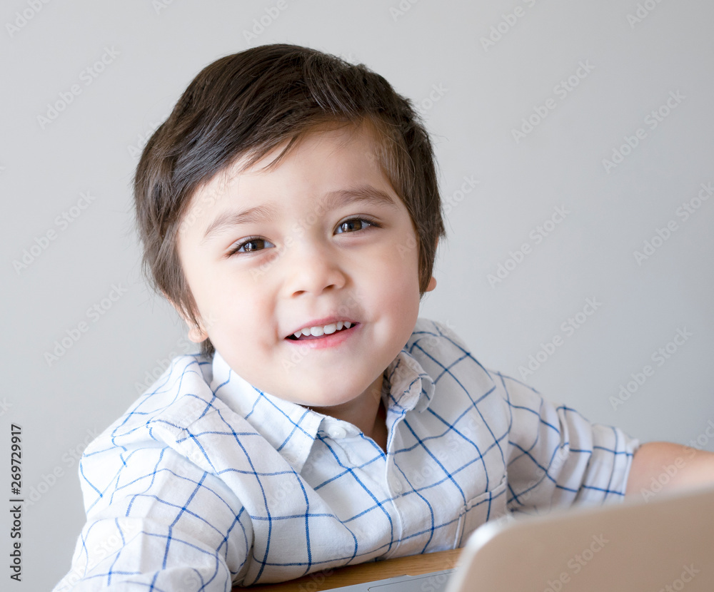 Cute little boy sitting on table playing game on computer, Smart kid looking at camera with smiling face, Children and Technology concept Cute little boy sitting on table playing game on computer, Smart kid looking at camera with smiling face, Children and Technology concept
