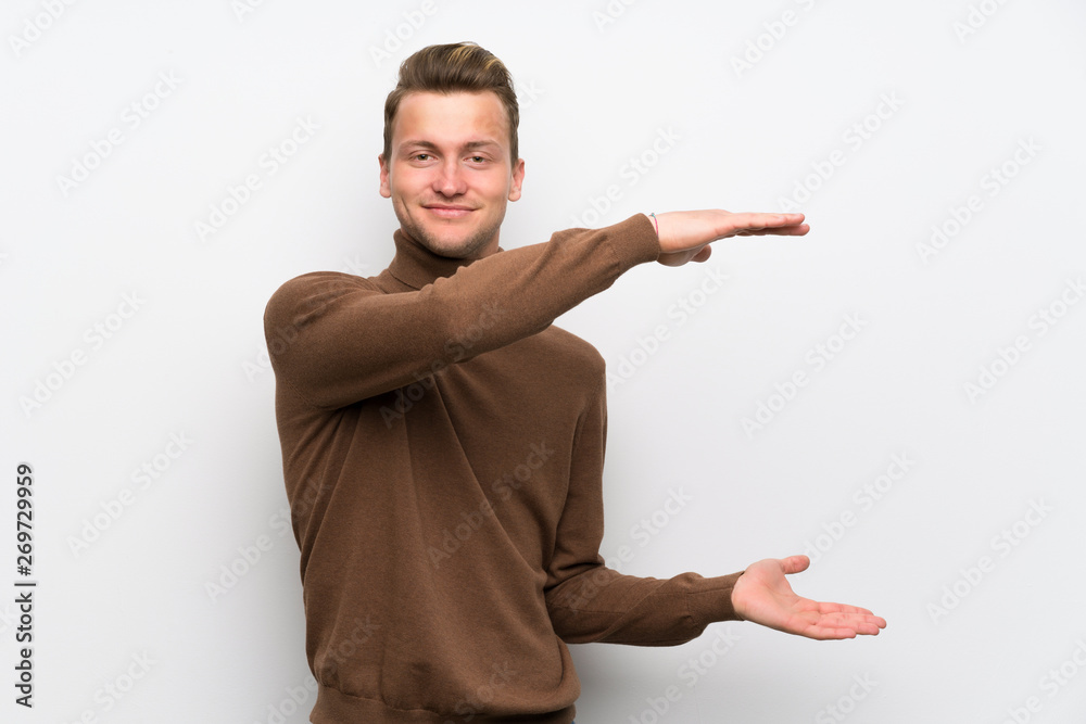 Blonde man over isolated white wall holding copyspace to insert an ad Blonde man over isolated white wall holding copyspace to insert an ad