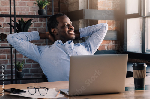 African man spending daytime in cafe with laptop open in relaxed pose, looking through window photo