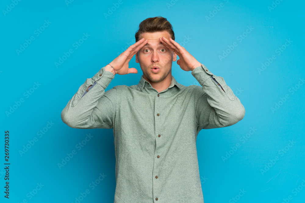 Blonde man over isolated blue wall with surprise expression Blonde man over isolated blue wall with surprise expression