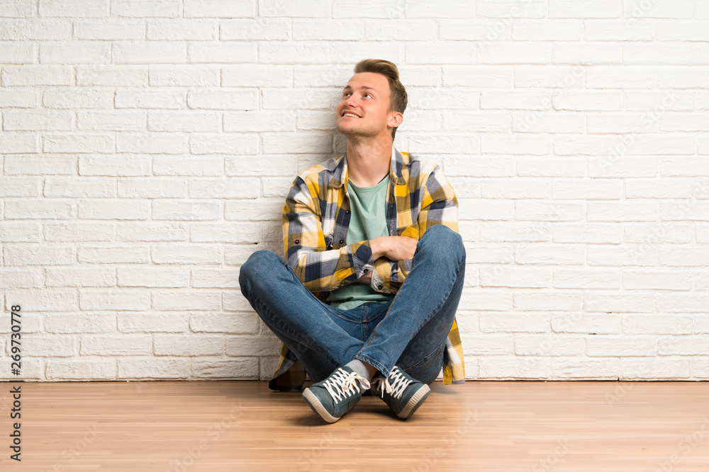 Blonde man sitting on the floor looking up while smiling Blonde man sitting on the floor looking up while smiling