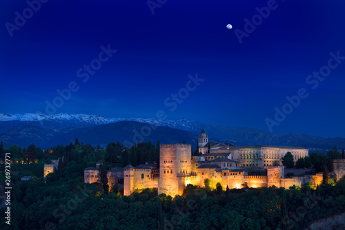 Moonrise over hilltop Alhambra Palace fortress complex at twilight Granada with Sierra Nevada Mountains