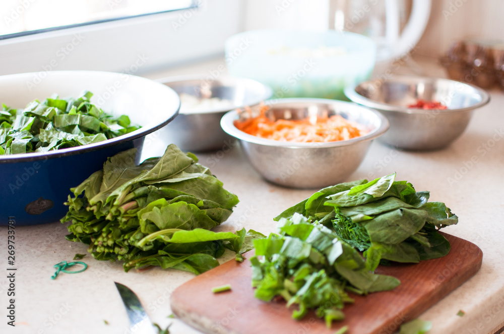 Bright fresh leaves of sorrel on a cutting board. Rustic style, against the background of vegetables in bowls: carrots, onions, pepper chopped.