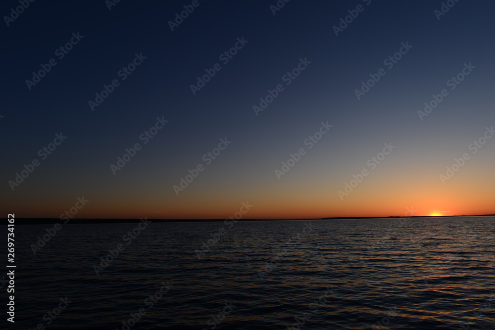 Sunset in the blue sky on the horizon above the water of the lake