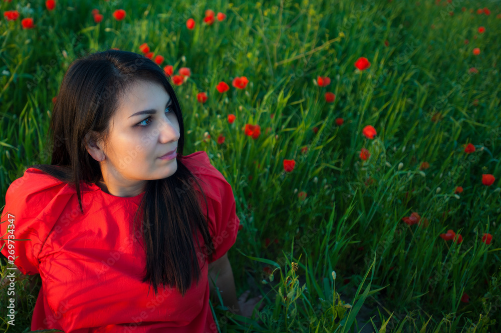 Naklejka premium Beautiful girl in red shirt has a relax in the field of red poppy flowers. Young woman enjoys of beauty nature.