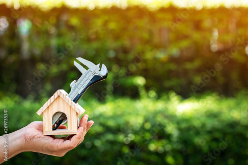 Man hand holding a wooden home with repairing on sunlight in the public park, Saving money and loan for construction real estate and house concept.