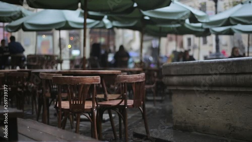Outdoors moody cafe with wet tables and chairs, rainy evening