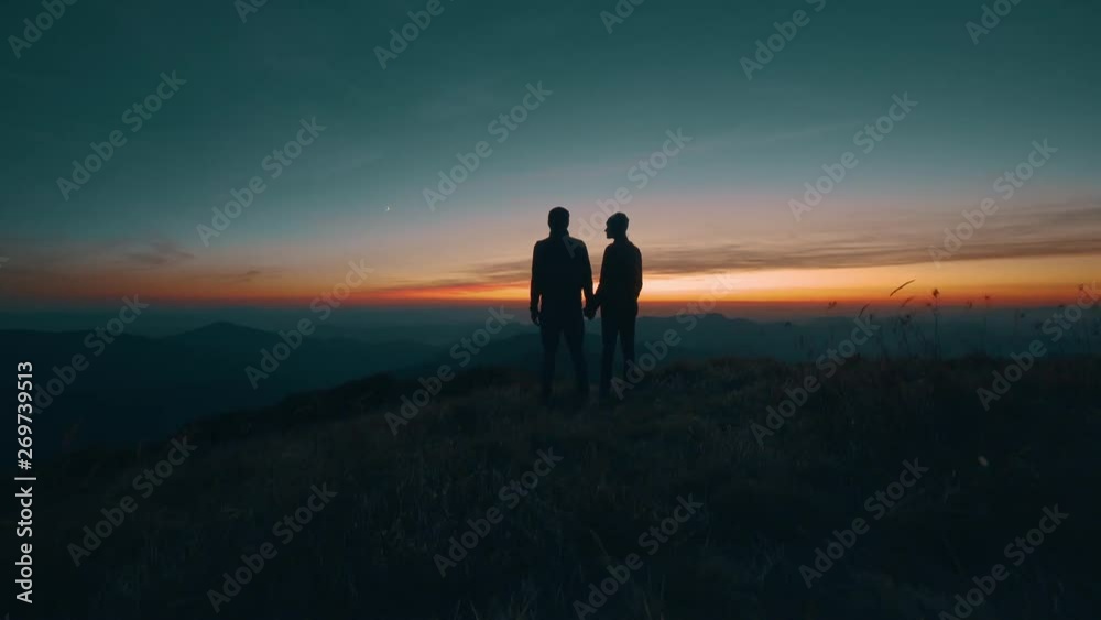 The couple standing on the mountain on a sunset background