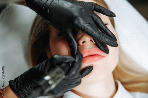 Young woman having permanent makeup on lips in beautician salon photo