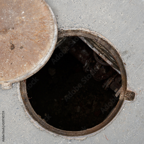 Closeup of an open manhole with a cover on the asphalt road. Top view of the sewer. Danger to people. Underground pipeline repair.