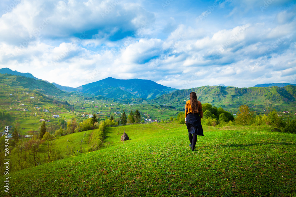 Fototapeta premium Girl walking through peaceful hills small village landscape area