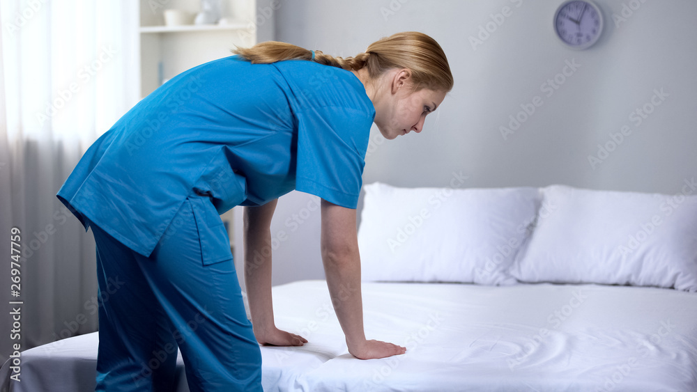 Young nurse preparing clean bed-linen in rehabilitation center, good service