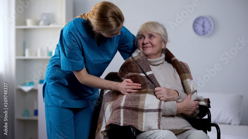Kind nurse covering with blanket handicapped old woman  hospital care  service