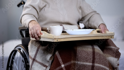 Old disabled woman holding tray with dinner, nursing home service, rehab center