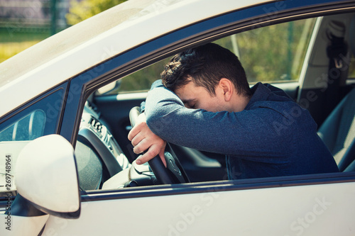 Obraz na plátne Nearly sleeping casual man keeps hand and head on the steering wheel being tired waiting in the traffic jam after work in the rush hour