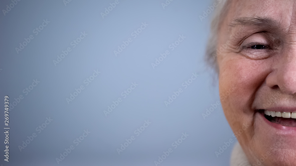 Fototapeta premium Half-face of smiling old woman grey background, social security, positive mood