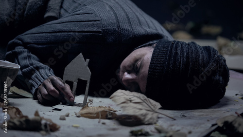 Freezing refugee sleeping on street and holding paper house, missing home