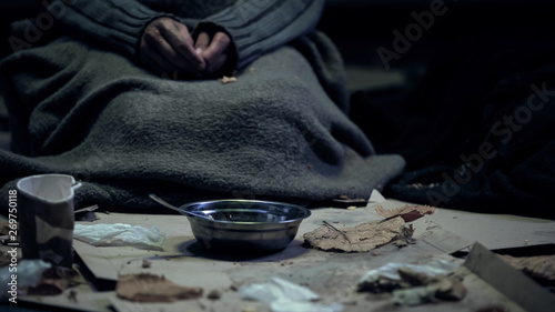 Poor person in dirty cloth sitting front of bowl, living on street, homelessness