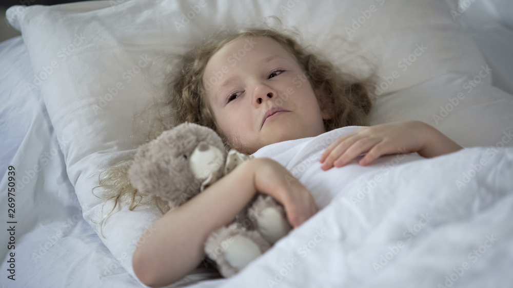 Sad little girl with toy crying in bed, unhappy sick child feeling lonely Sad little girl with toy crying in bed, unhappy sick child feeling lonely