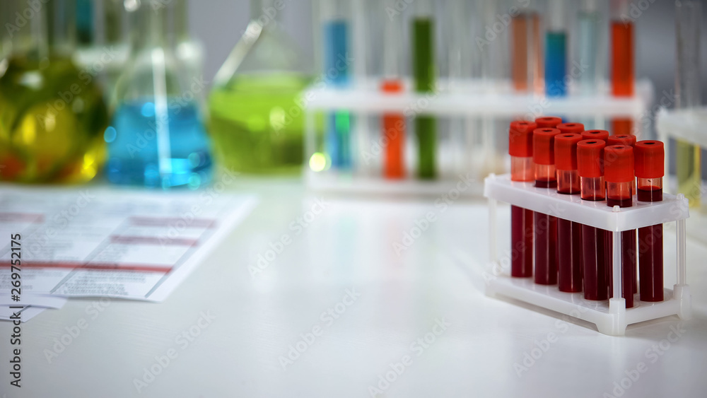 Medical lab worker holding capsule, blood samples on background, pharmaceuticals Medical lab worker holding capsule, blood samples on background, pharmaceuticals