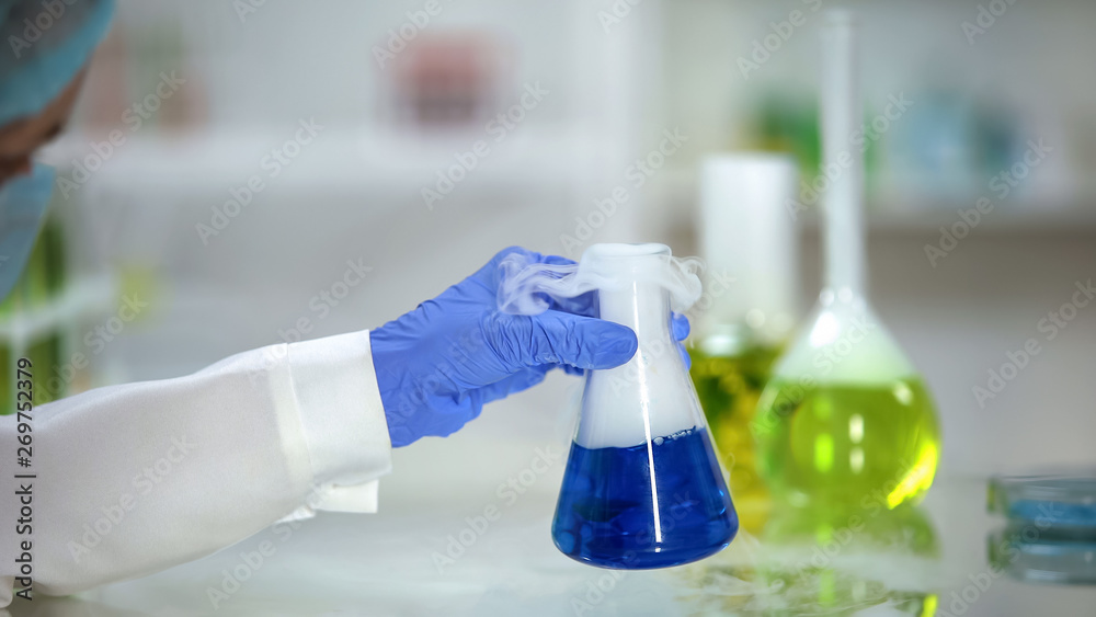 Lab assistant checking reaction in flask with blue substance emitting smoke Lab assistant checking reaction in flask with blue substance emitting smoke