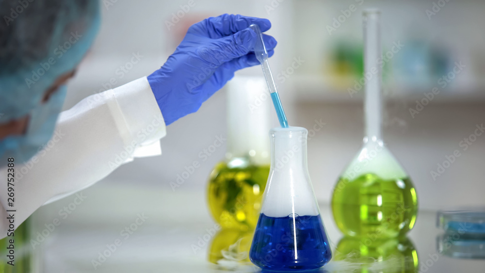 Chemist taking blue substance sample from flask, washing agent analysis, test Chemist taking blue substance sample from flask, washing agent analysis, test