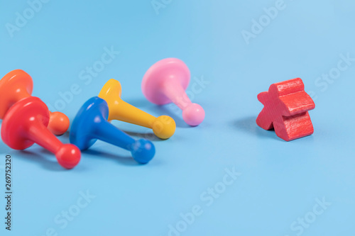 A wooden red figure stands in front of several fallen plastic multicolored ones