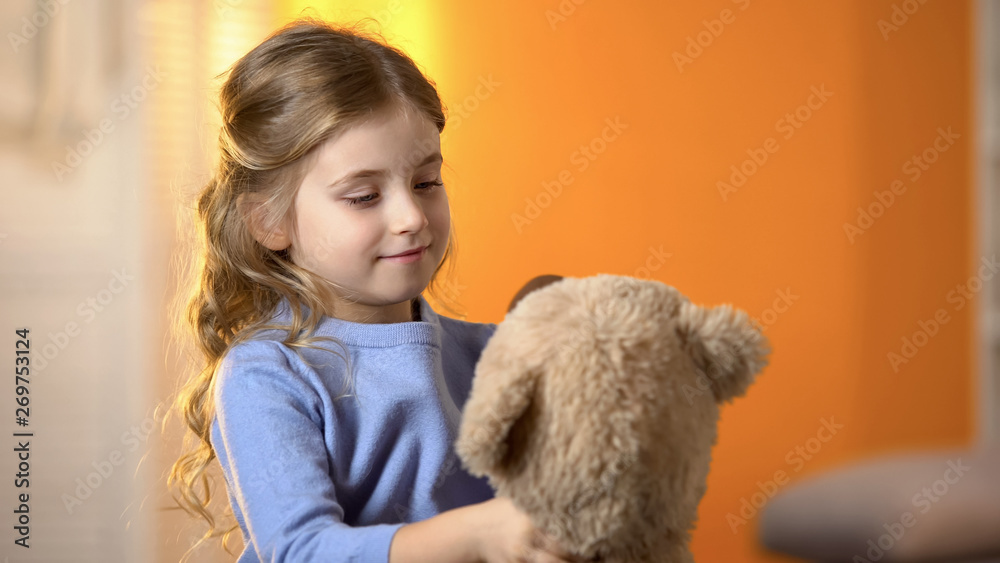 Preschool girl looking at teddy bear, playing with toy, happy little princess