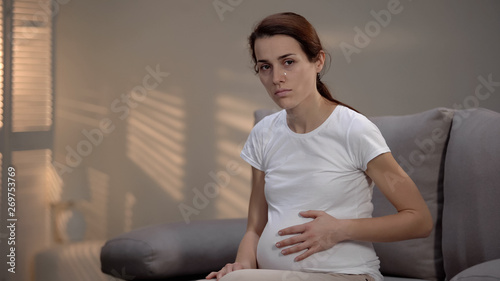 Hopeless crying pregnant marital mistreatment victim stroking belly, depression