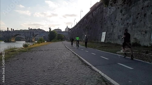 Slow Motion A man jogs In Rome on the bicycle lane near the Tiber river with view of St. Peter dome at distance and the sant'angelo bridge