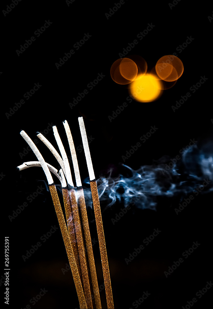 varios palos de incienso encendidos desprendiendo humo en un fondo negro