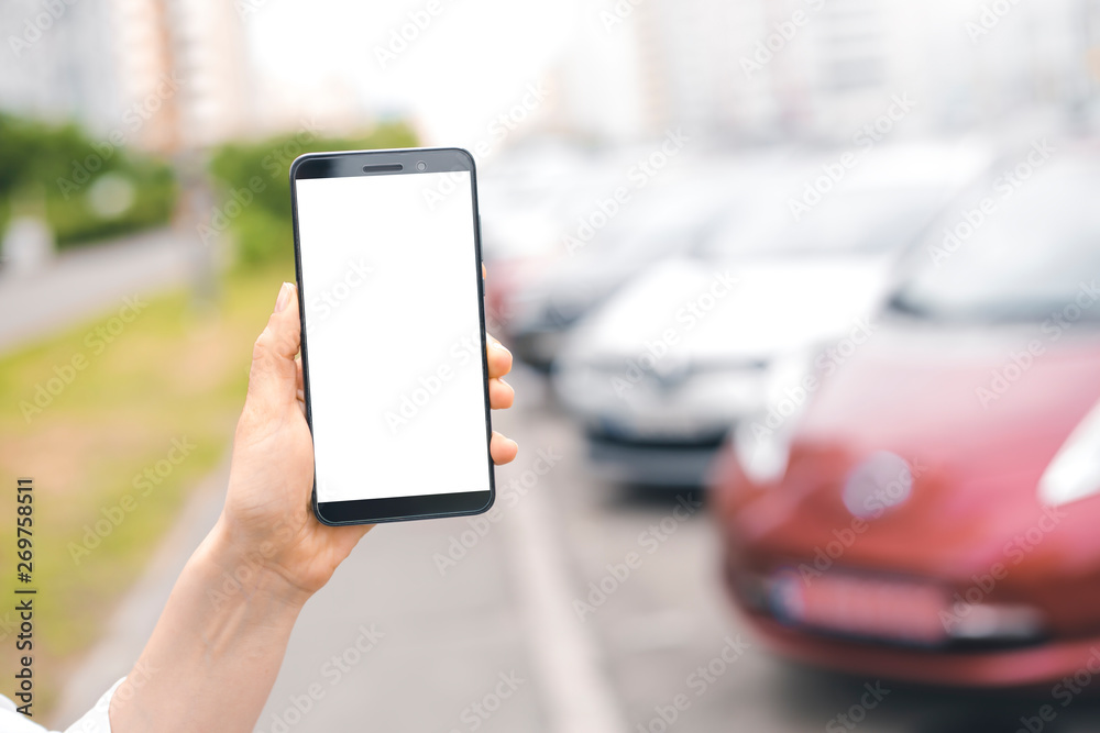 Smartphone in hand with a white screen on the background of parked cars. Smartphone in hand with a white screen on the background of parked cars.