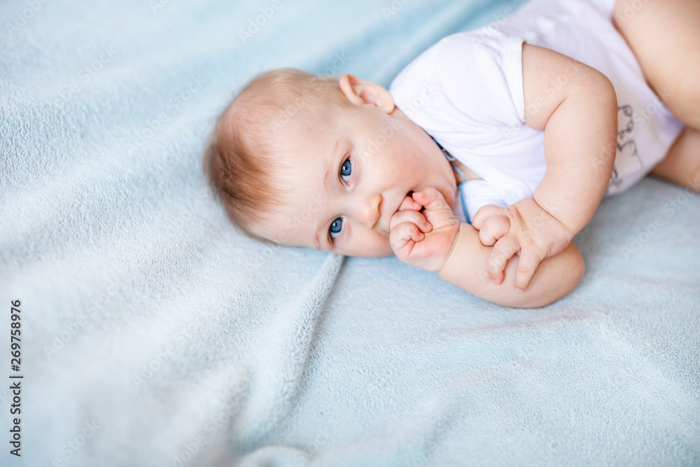 Adorable baby boy in white sunny bedroom. Newborn child relaxing on a blue bed. Nursery for young children. Newborn kid during tummy time with toys at a window Adorable baby boy in white sunny bedroom. Newborn child relaxing on a blue bed. Nursery for young children. Newborn kid during tummy time with toys at a window