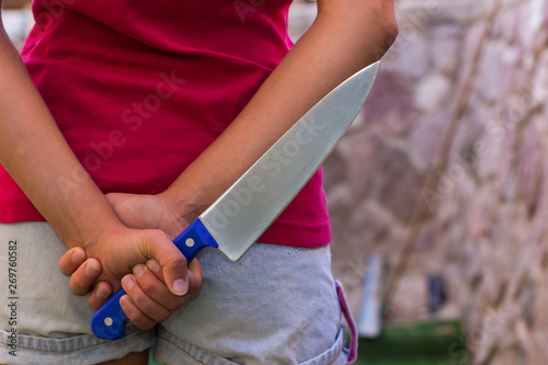 female violence concept photography of kitchen knife behind back in woman hand, copy space