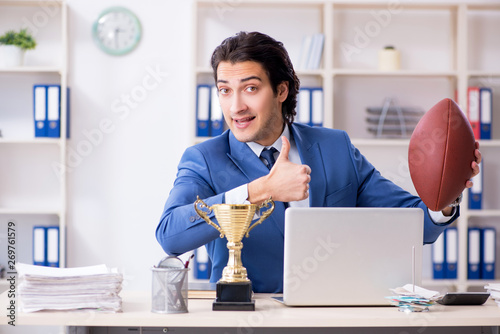 Young handsome businessman with rugby ball in the office