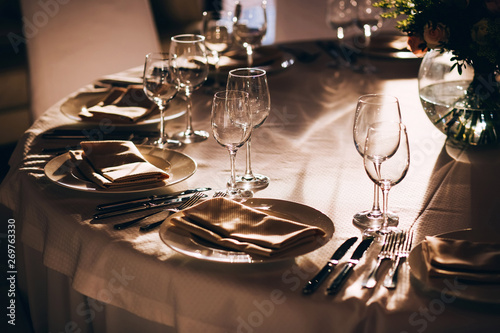 served table with white tablecloth. white plates, wine glass, fork, knife