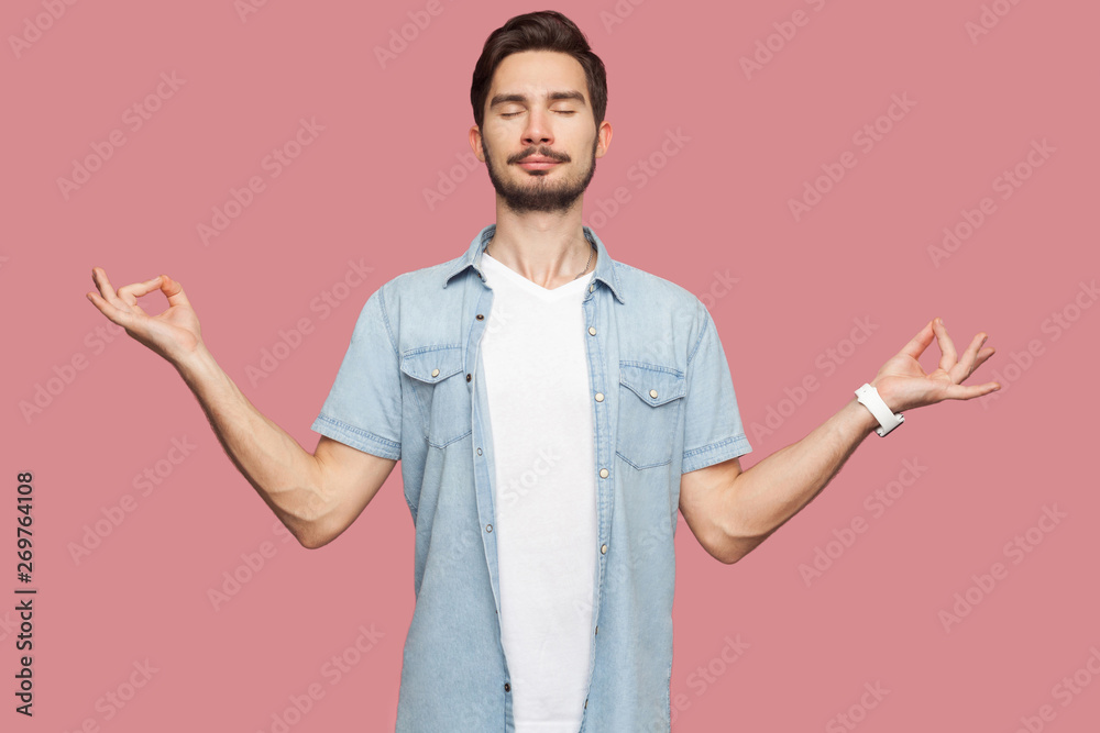 Portrait of calm relaxed handsome bearded young man in blue casual style shirt standing with raised arms and doing yoga meditating exercise. indoor studio shot, isolated on pink background. Portrait of calm relaxed handsome bearded young man in blue casual style shirt standing with raised arms and doing yoga meditating exercise. indoor studio shot, isolated on pink background.