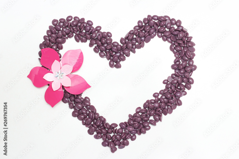 wax for depilation in granules laid out in the shape of a heart on  white background with  flower