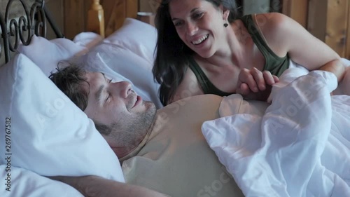 Happy couple lying in bed together waking up and starting their day talking