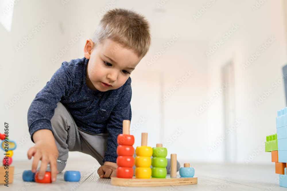 Small boy playing with wood brain teaser toys on the wooden floor at home Small boy playing with wood brain teaser toys on the wooden floor at home
