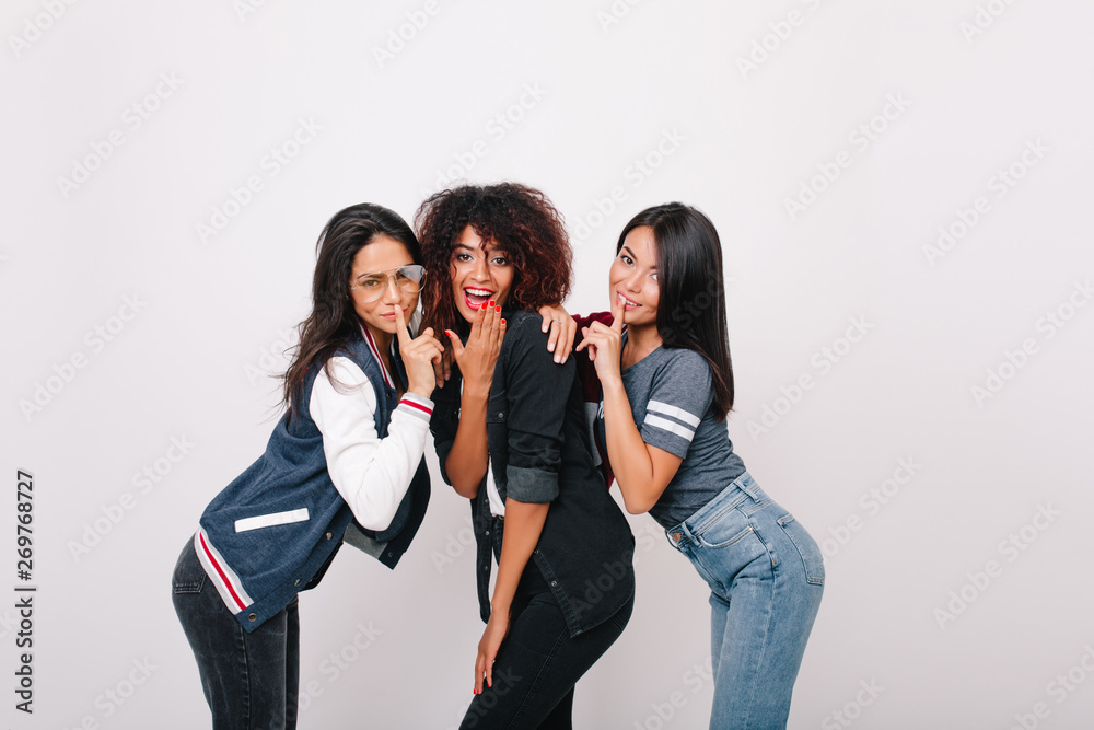 Enchanting african girl with red manicure cover mouth with hand while posing beside university mates. Fascinating latin young woman with shiny hair having fun with friends and laughing. Enchanting african girl with red manicure cover mouth with hand while posing beside university mates. Fascinating latin young woman with shiny hair having fun with friends and laughing.
