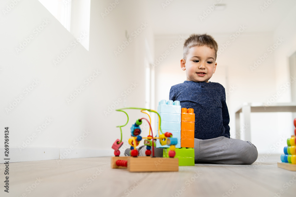 Small boy playing with plastic brick block toys on the wooden floor at home Small boy playing with plastic brick block toys on the wooden floor at home