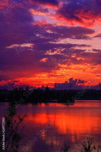 Amazing sunset on a lake with vegetation silhouette in foreground.  Colorful cloudy sky in perspective over water in the countryside © Bruno