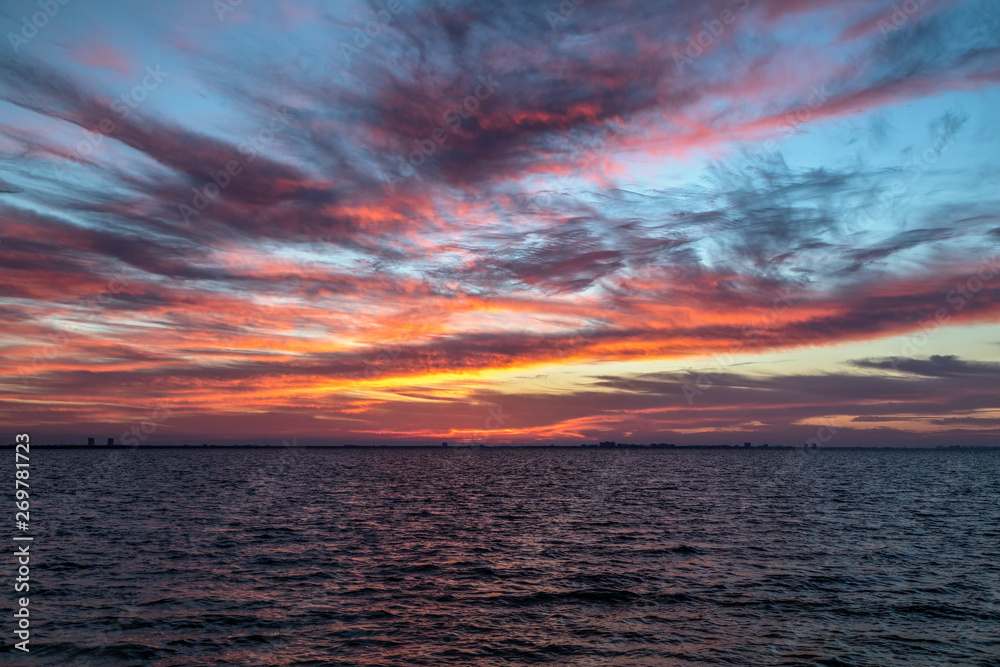 Fototapeta premium San Carlos Bay Sunrise - The rising sun paints a cloudy morning sky with vivid colors over San Carlos Bay with Fort Myers Beach, Florida on the horizon