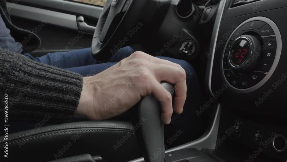 Urban man using transmission and driving speed. Man hand on automatic transmission car lever. Driver man controls auto and switch gears a lot. Close up of gear shift in car. Low angle shot. Urban man using transmission and driving speed. Man hand on automatic transmission car lever. Driver man controls auto and switch gears a lot. Close up of gear shift in car. Low angle shot.