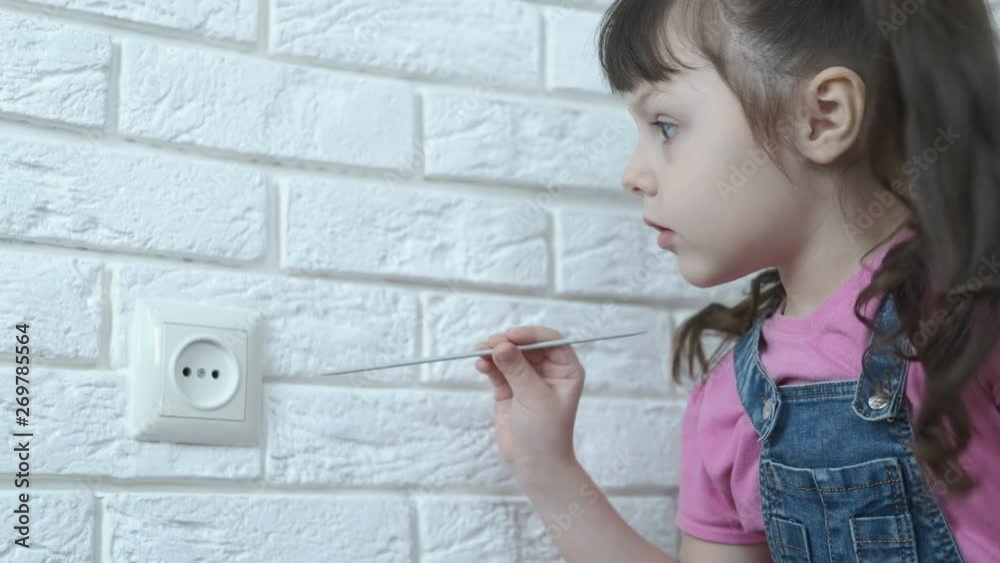 The child is in danger. A cute little girl puts a knitting needle into an outlet. The child is in danger. A cute little girl puts a knitting needle into an outlet.