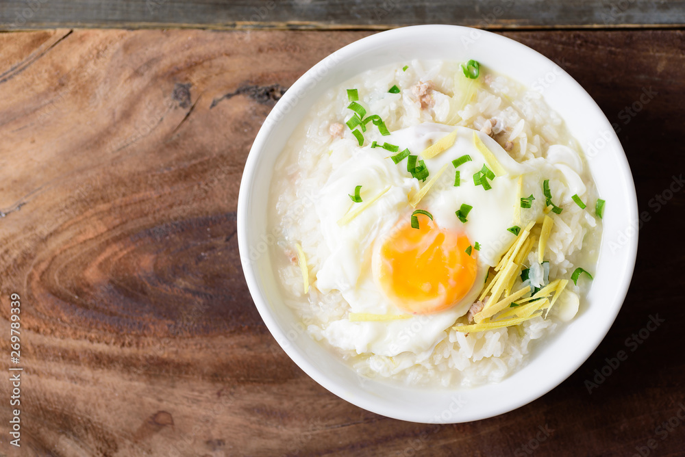 Thai rice soup or soft-boiled rice with pork and egg in the bowl on wooden background Thai rice soup or soft-boiled rice with pork and egg in the bowl on wooden background
